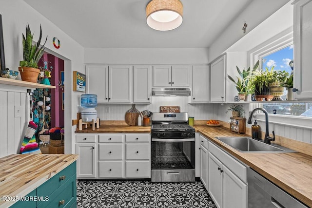 kitchen with under cabinet range hood, stainless steel appliances, butcher block countertops, a sink, and white cabinets