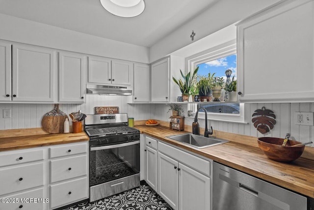 kitchen with butcher block countertops, appliances with stainless steel finishes, under cabinet range hood, white cabinetry, and a sink