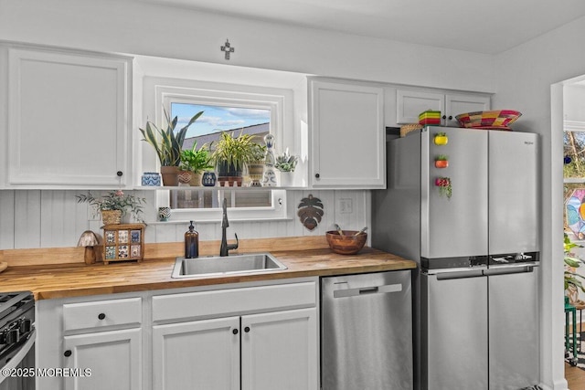 kitchen with wooden counters, appliances with stainless steel finishes, a sink, and white cabinets