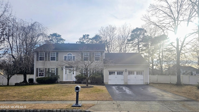 colonial-style house with an attached garage, aphalt driveway, a front yard, and fence