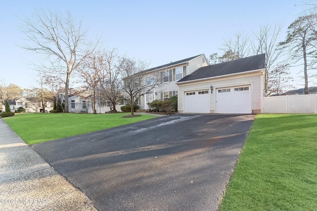 colonial inspired home featuring aphalt driveway, a garage, fence, a residential view, and a front lawn