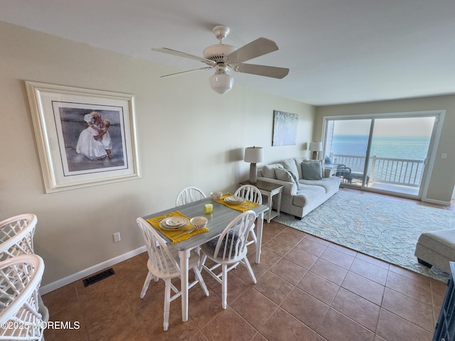 tiled dining area with a ceiling fan, visible vents, a water view, and baseboards