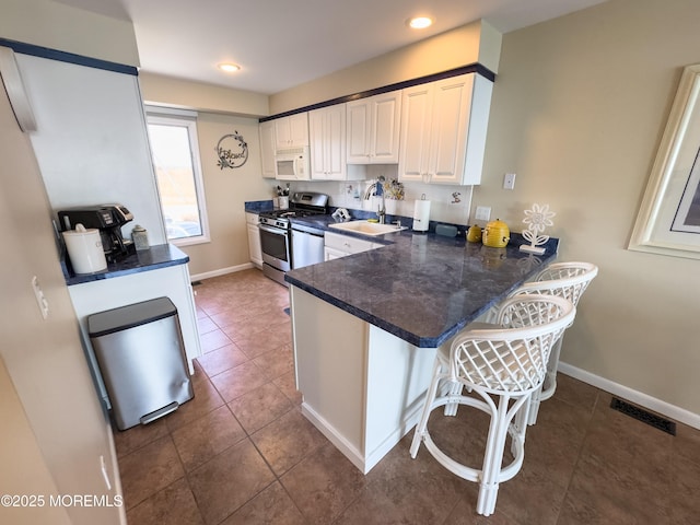 kitchen featuring white microwave, a breakfast bar area, stainless steel gas range oven, a peninsula, and white cabinets