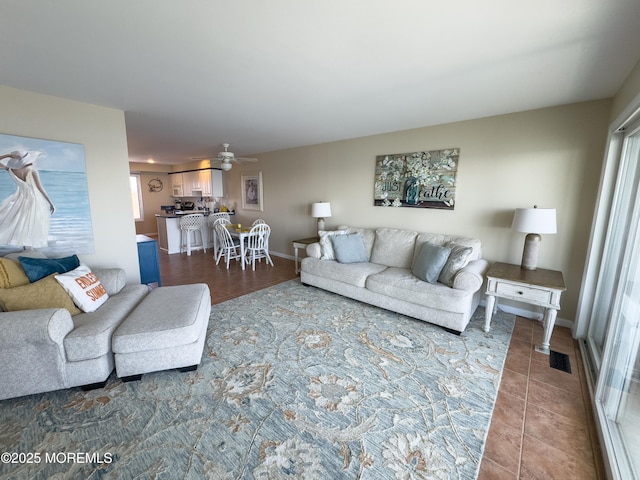 living room with a ceiling fan, dark tile patterned floors, visible vents, and baseboards