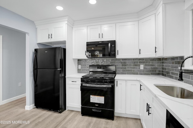 kitchen with light wood-style floors, light stone counters, black appliances, white cabinetry, and a sink