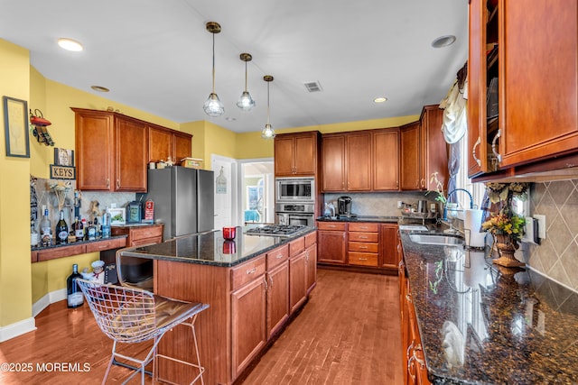 kitchen featuring a kitchen island, visible vents, a sink, appliances with stainless steel finishes, and decorative light fixtures