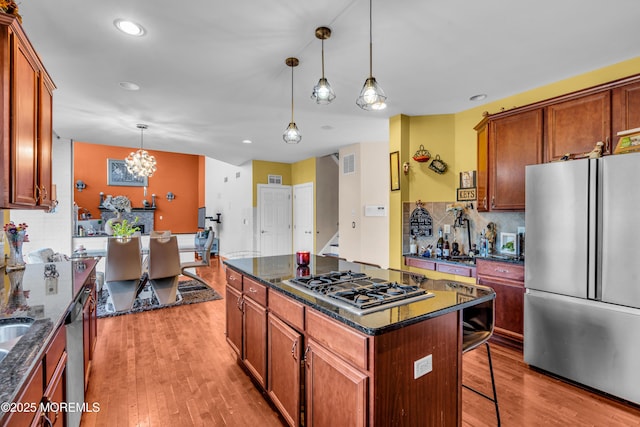 kitchen with a breakfast bar, pendant lighting, stainless steel appliances, a kitchen island, and dark stone countertops