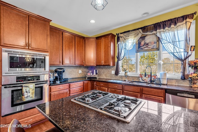 kitchen with backsplash, appliances with stainless steel finishes, a healthy amount of sunlight, a sink, and dark stone counters