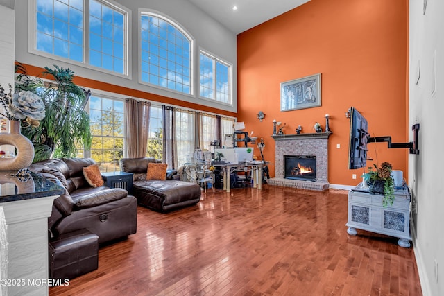 living room featuring a fireplace, a towering ceiling, baseboards, and wood finished floors