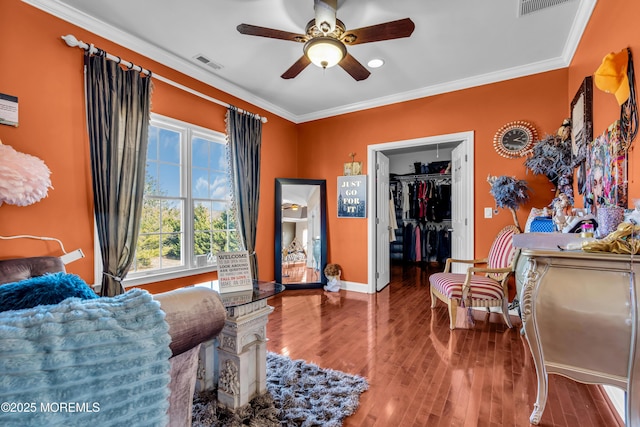 bedroom featuring a walk in closet, crown molding, visible vents, wood finished floors, and baseboards