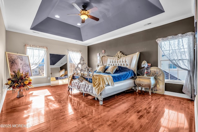 bedroom featuring crown molding, a raised ceiling, visible vents, wood finished floors, and baseboards