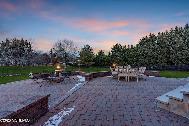 patio terrace at dusk with a yard, a fire pit, and fence