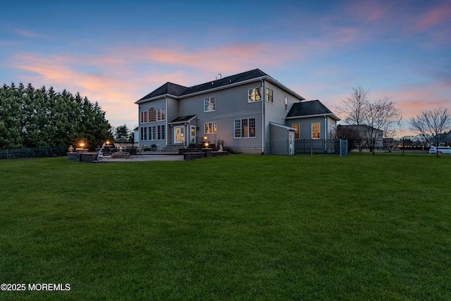 back of house at dusk featuring a fire pit, a lawn, a patio area, and fence