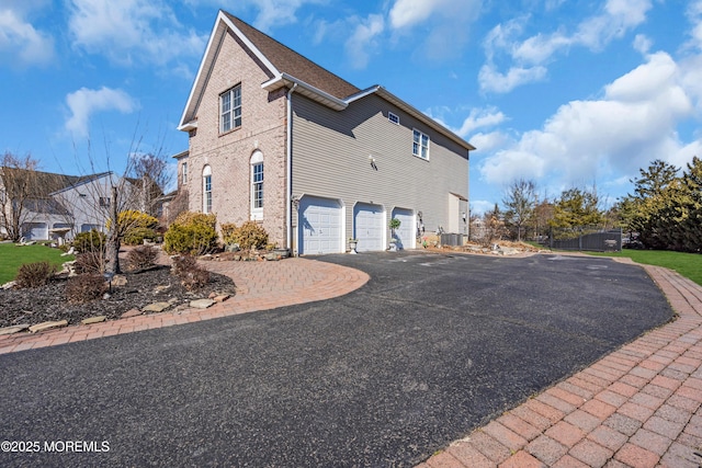 view of home's exterior featuring a garage, aphalt driveway, cooling unit, and brick siding