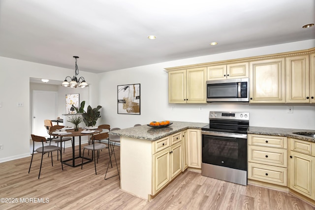 kitchen with light wood finished floors, appliances with stainless steel finishes, a peninsula, cream cabinets, and pendant lighting