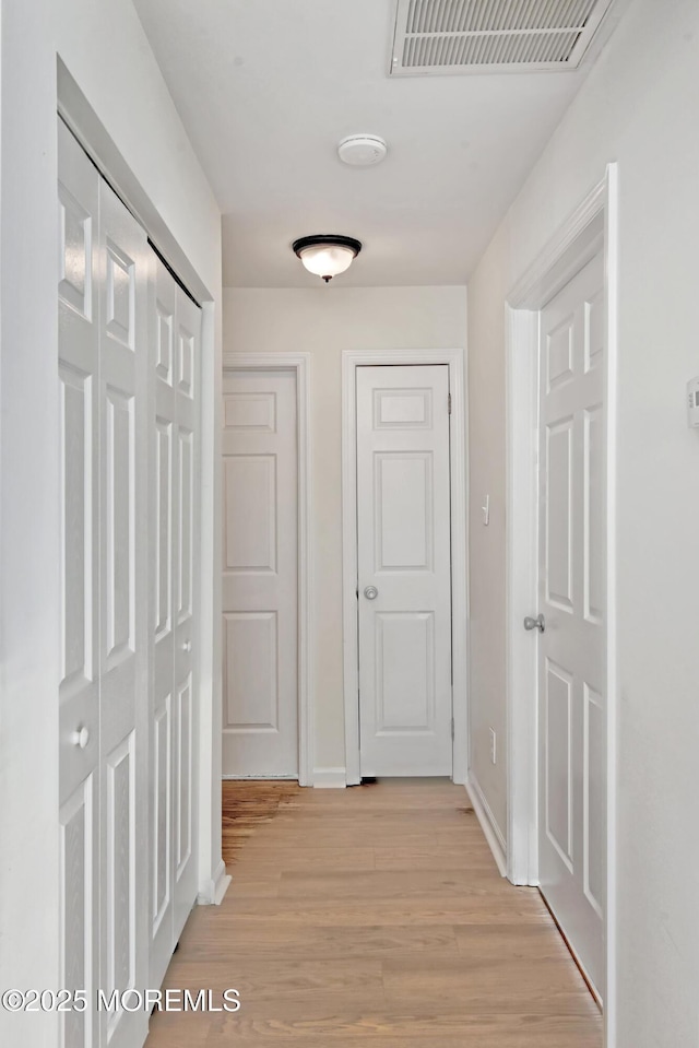 hallway featuring baseboards, visible vents, and light wood-style floors