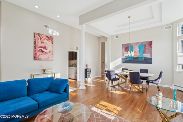 living area with ornate columns, visible vents, a raised ceiling, and wood finished floors