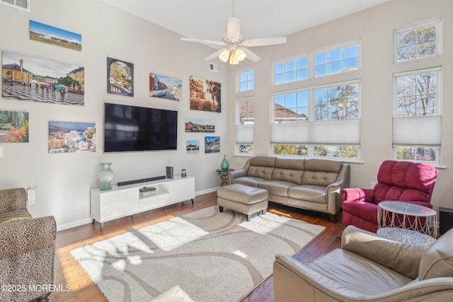 living area featuring baseboards, visible vents, ceiling fan, wood finished floors, and a high ceiling