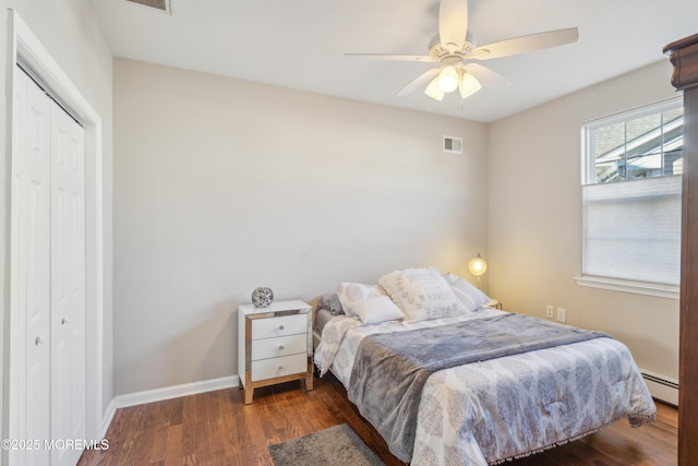 bedroom with a closet, visible vents, baseboard heating, dark wood-type flooring, and baseboards