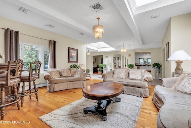 living area with a skylight, a baseboard radiator, visible vents, light wood-style floors, and beamed ceiling