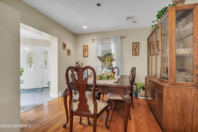 dining area with light wood finished floors, baseboards, visible vents, and a textured ceiling