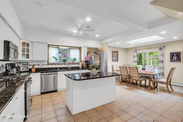 kitchen with appliances with stainless steel finishes, white cabinets, glass insert cabinets, and a kitchen island