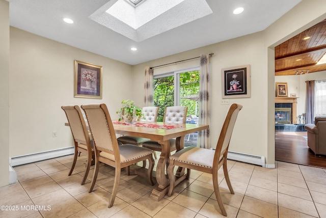 dining space featuring a glass covered fireplace, a baseboard radiator, a skylight, and light tile patterned flooring