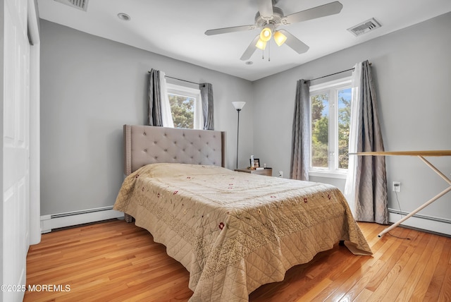 bedroom with light wood-type flooring, a baseboard radiator, multiple windows, and visible vents