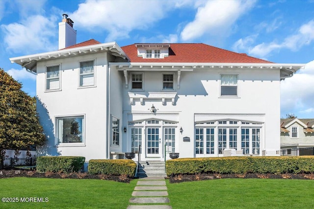 rear view of house featuring a lawn, a chimney, fence, and stucco siding