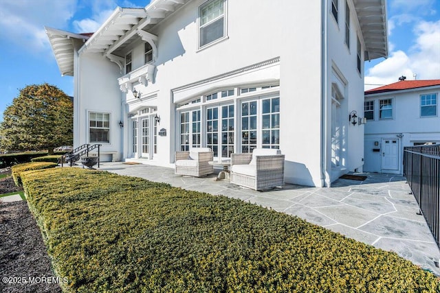 rear view of property featuring french doors, a patio, fence, and stucco siding