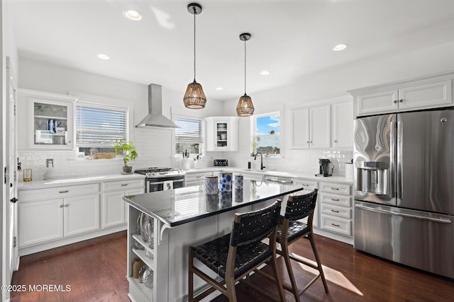 kitchen with dark wood-style floors, a breakfast bar, appliances with stainless steel finishes, a sink, and wall chimney range hood