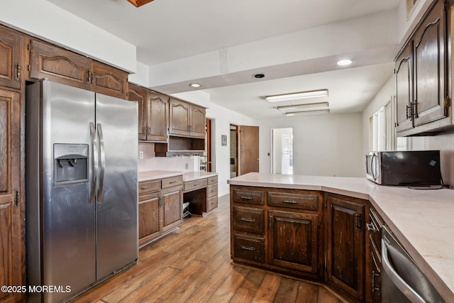 kitchen with hardwood / wood-style flooring, stainless steel appliances, a peninsula, dark brown cabinets, and light countertops