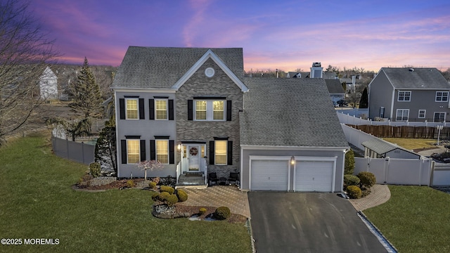 traditional-style house featuring aphalt driveway, a front yard, fence, and an attached garage