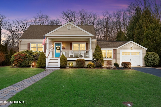 view of front of house featuring a shingled roof, covered porch, a lawn, a garage, and driveway