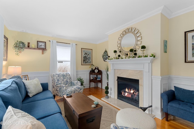 living area featuring a wainscoted wall, light wood finished floors, a fireplace, and crown molding