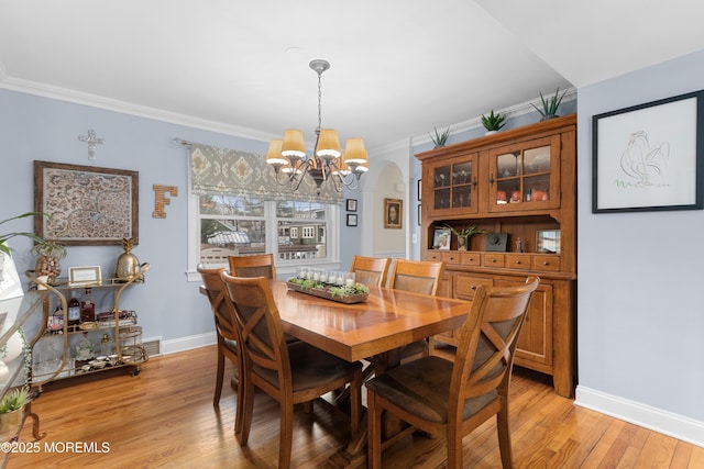 dining space with arched walkways, crown molding, an inviting chandelier, light wood-style floors, and baseboards