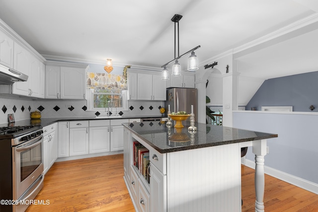 kitchen featuring appliances with stainless steel finishes, light wood-style floors, white cabinets, a kitchen island, and dark stone countertops