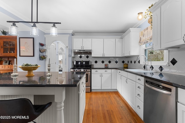 kitchen featuring white cabinetry, stainless steel appliances, a sink, and decorative light fixtures