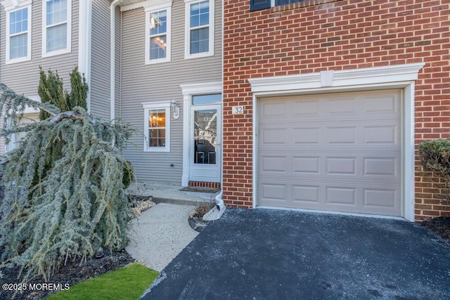 entrance to property with a garage, brick siding, and driveway