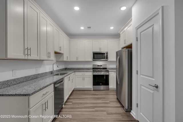 kitchen with light stone counters, recessed lighting, stainless steel appliances, a sink, and white cabinets