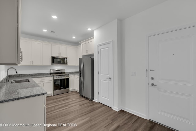 kitchen with a sink, white cabinetry, appliances with stainless steel finishes, light wood finished floors, and dark stone countertops