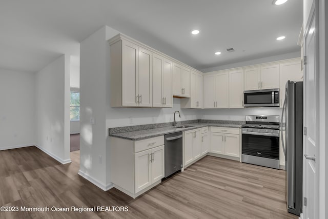 kitchen with light wood finished floors, appliances with stainless steel finishes, a sink, and light stone countertops