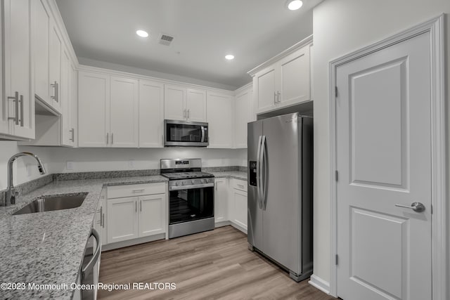 kitchen with a sink, white cabinetry, appliances with stainless steel finishes, light stone countertops, and light wood finished floors