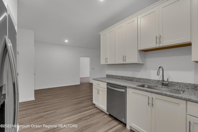 kitchen with light stone counters, light wood-style flooring, appliances with stainless steel finishes, white cabinetry, and a sink