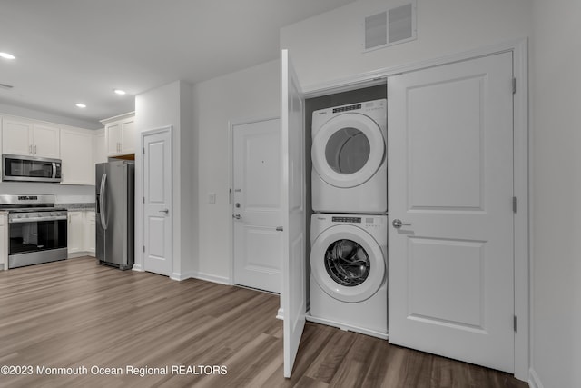 clothes washing area with stacked washer and dryer, laundry area, light wood finished floors, visible vents, and recessed lighting