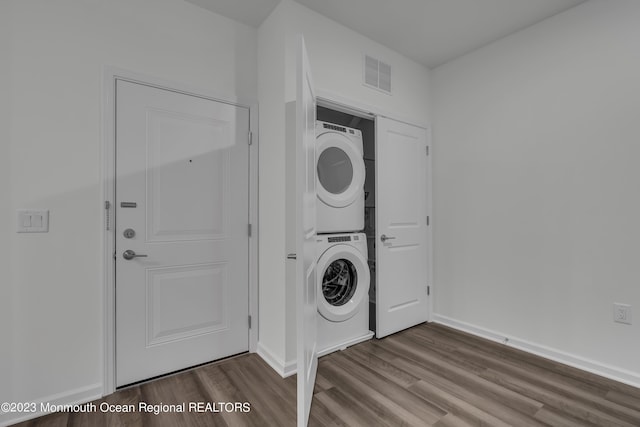 laundry room with laundry area, stacked washer / dryer, wood finished floors, visible vents, and baseboards