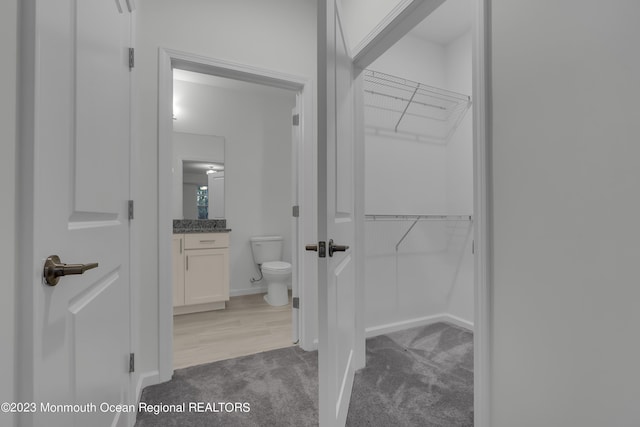 bathroom with toilet, baseboards, a walk in closet, and vanity