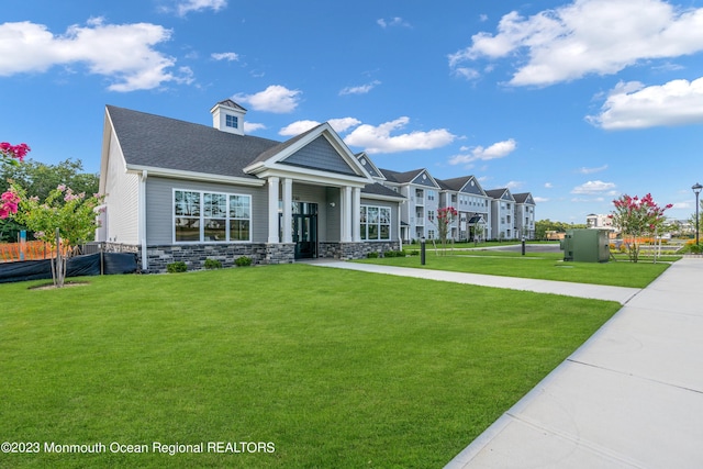 view of front of property featuring stone siding, a shingled roof, fence, and a front lawn