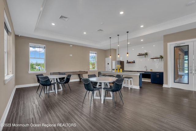 dining space with dark wood-type flooring, visible vents, a raised ceiling, and a wealth of natural light