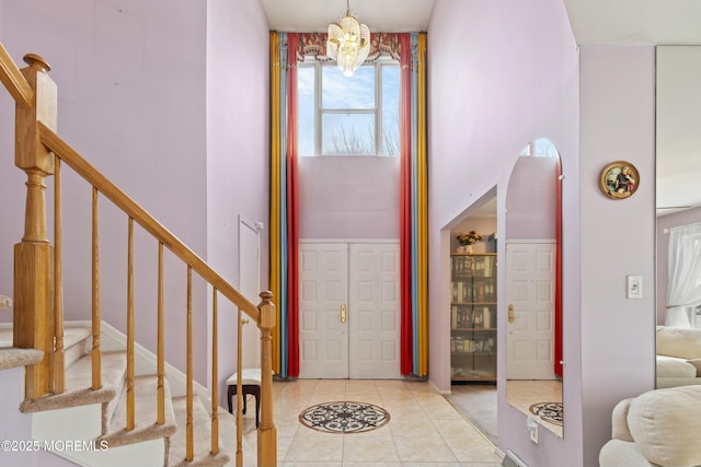 entryway with light tile patterned floors, stairs, a towering ceiling, and a notable chandelier